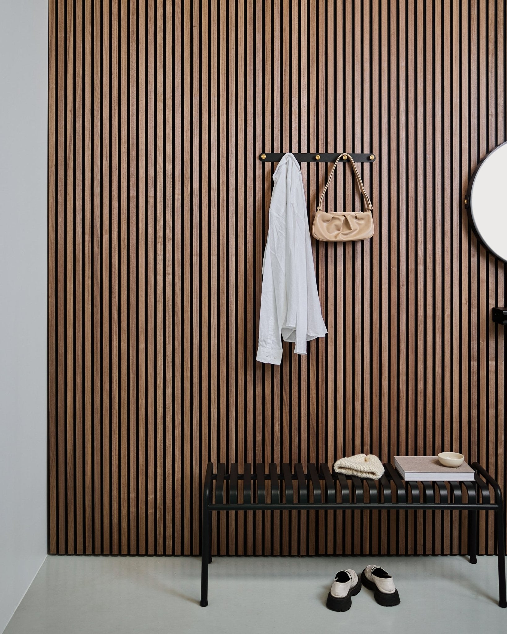 El perchero con ganchos WoodUpp Norr en black y brass sostiene una camisa blanca y un bolso beige sobre un banco black; debajo, unas zapatillas blancas están colocadas con cuidado.